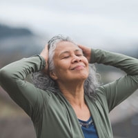 Older woman of color with eyes closed, taking deep breaths outdoors