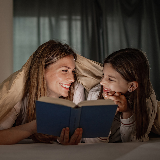 Mom and daughter reading book in bed
