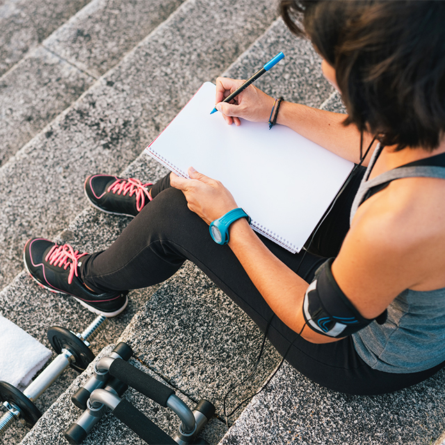 Woman writing fitness goals near workout gear