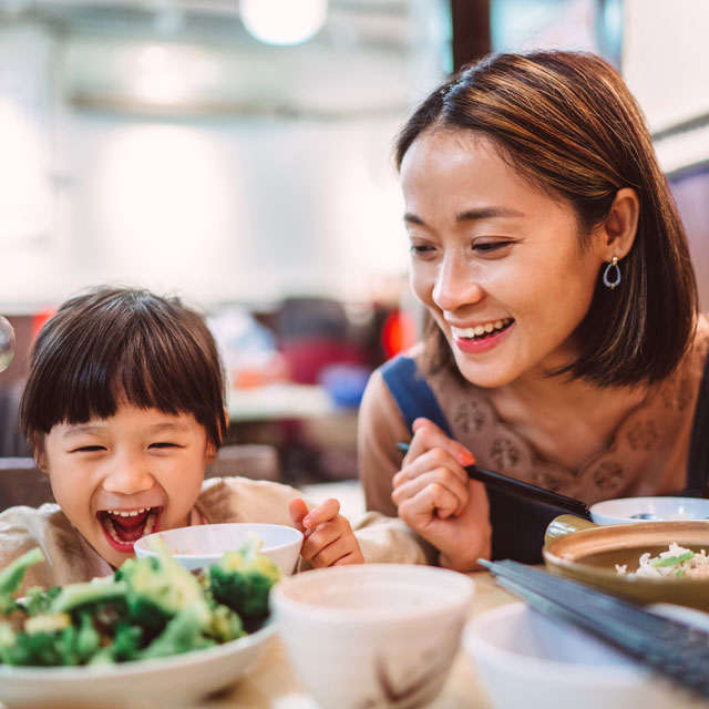 Asian-American mother and daughter eat a meal at a restaurant.