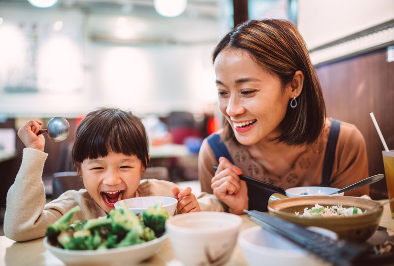 Asian-American mother and daughter eat a meal at a restaurant.
