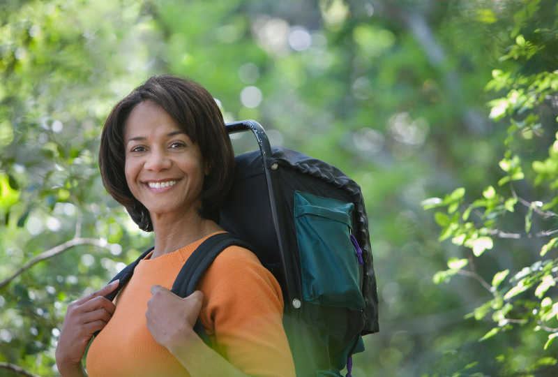 Black woman walking in woods wearing backpack