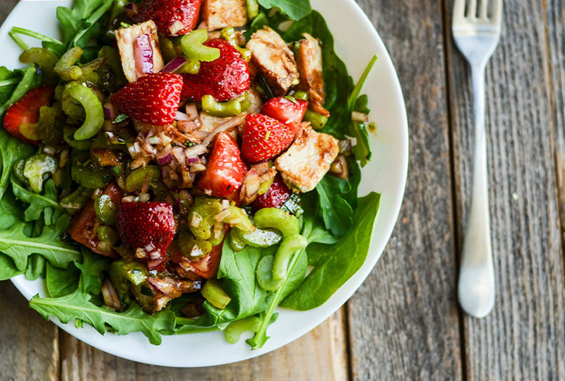 White bowl with greens, cooked chicken and strawberries.