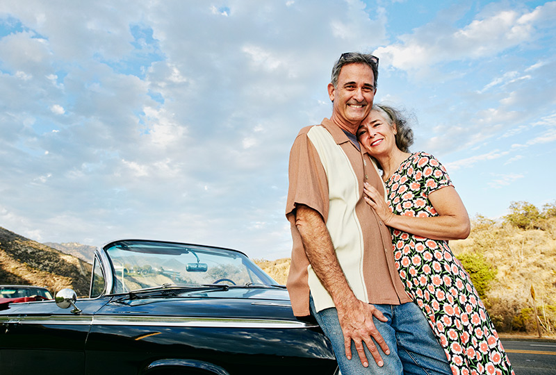 Older couple pose next to vintage sports convertible car.