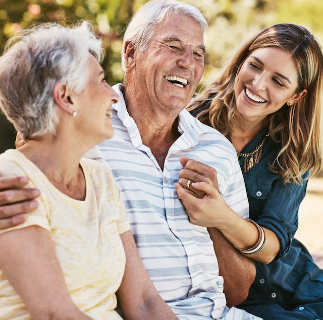 An adult woman laughs and hugs her parents.