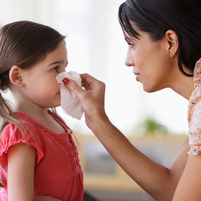 A mother helps her young daughter blow her nose with a tissue.