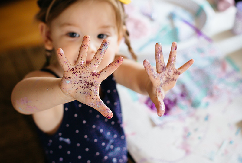 Young girl holds up both hands covered in glitter.