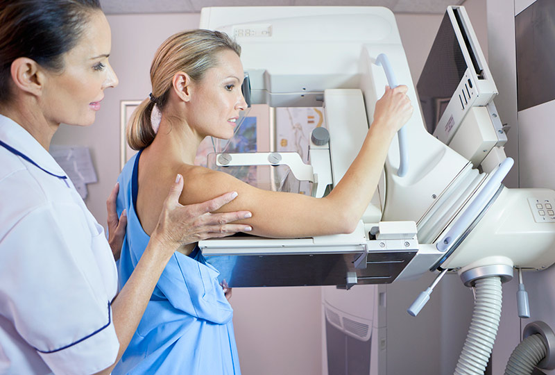 An imaging technician prepares a young woman for a mammogram