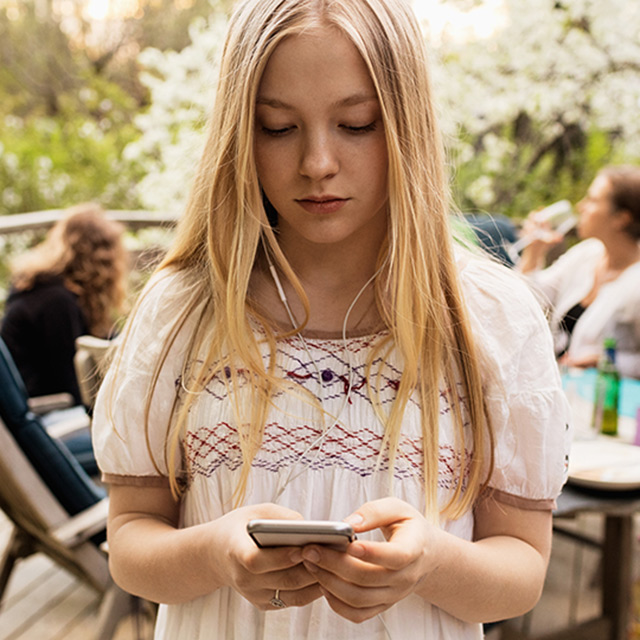 Teen girl looking at phone screen at family gathering.
