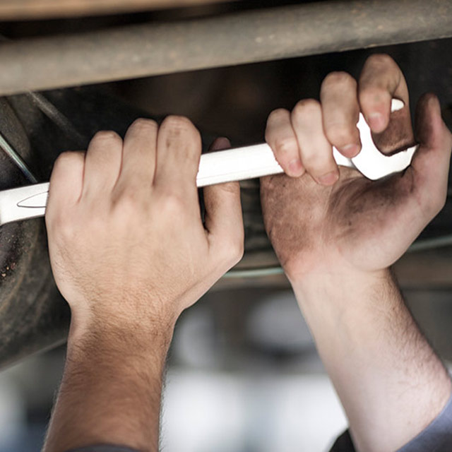 Man's hands work with a wrench on a car part.