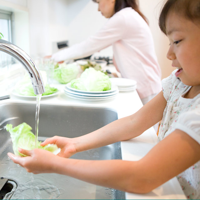 Young girl safely rinsing lettuce under cool water to prevent scalding burn injury.