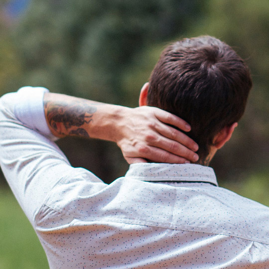 Man with a tattooed arm, seen from behind, rubbing his neck