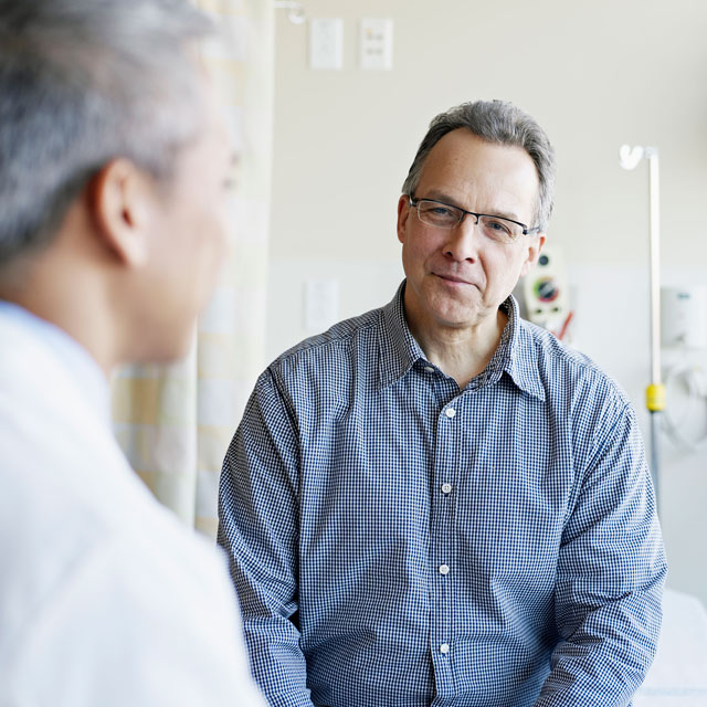 A middle-aged man faces the camera during a doctor's appointment, with the doctor's back to the camera.