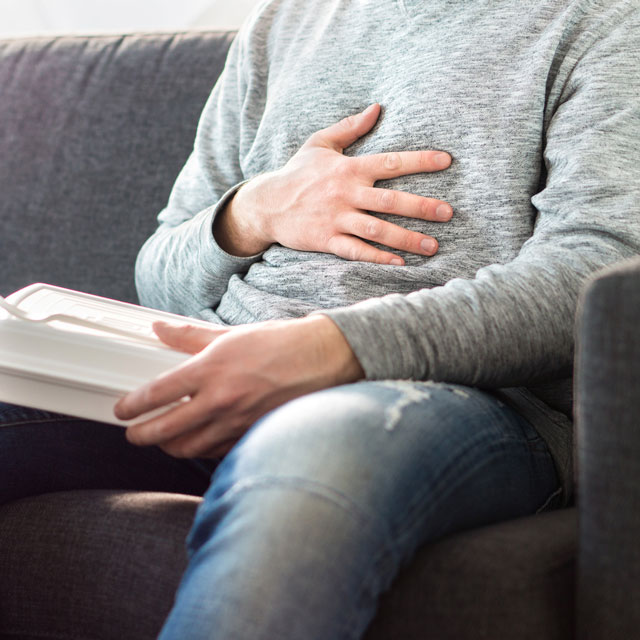 Man sitting on couch after eating a meal feeling for constant heartburn.