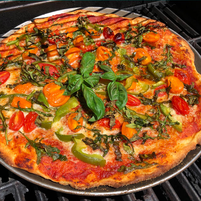 Grilled pizza topped with fresh vegetables and herbs.