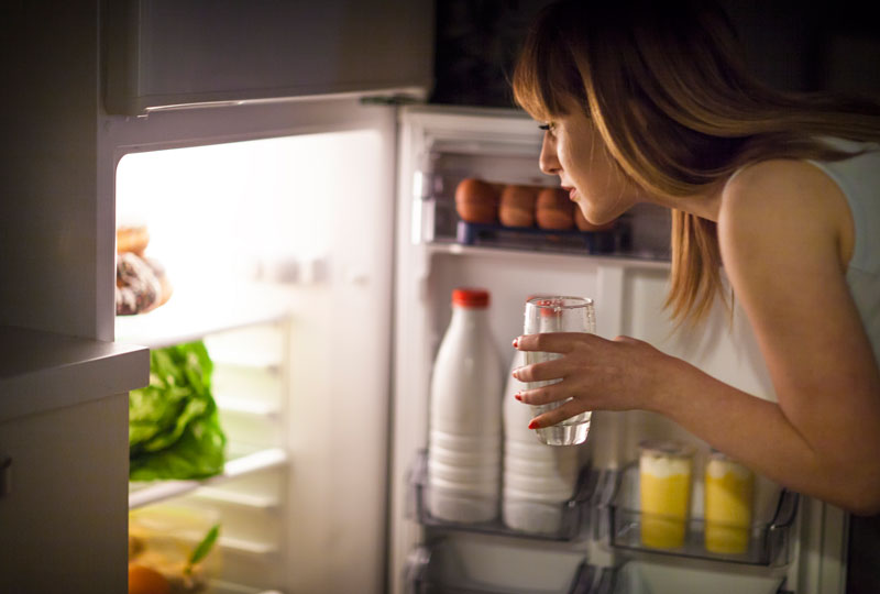 Woman looking into fridge looking for better alternatives to stop snacking at night.