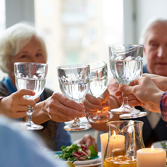 A family raises glasses of water in a toast to begin a meal.