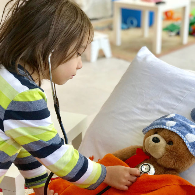 A young boy uses a stethoscope to listen to a teddy bear's heart.
