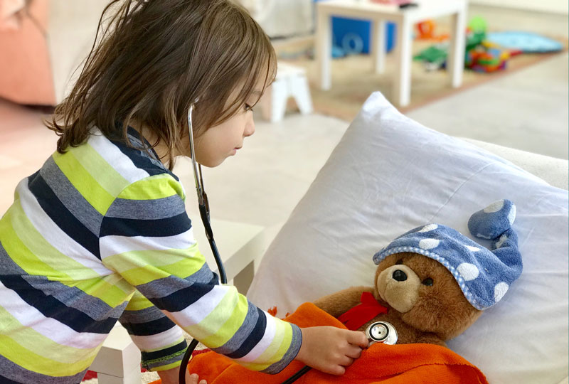 A young boy uses a stethoscope to listen to a teddy bear's heart.