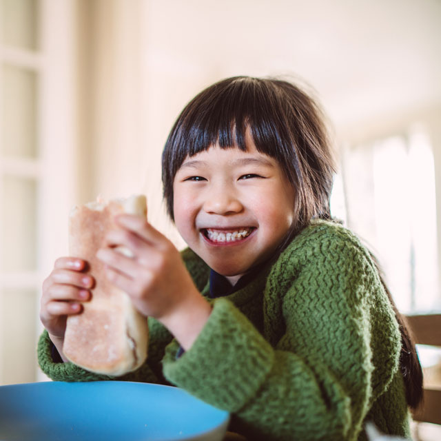 Asian girl eats a breakfast burrito sitting at a table at home.