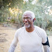 Older African American man walking outdoors wearing earbuds