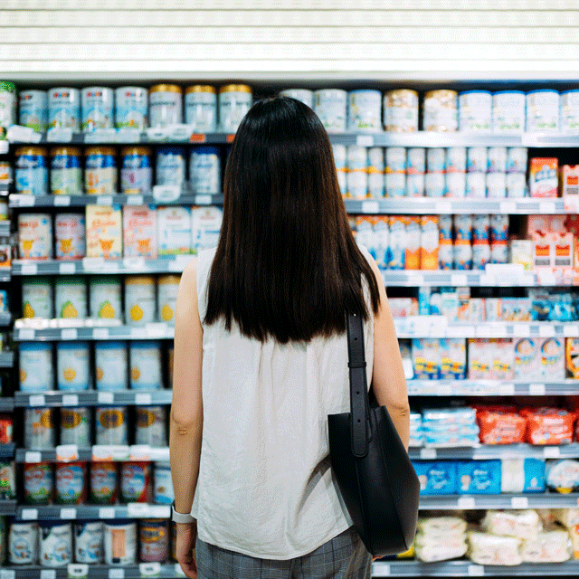 Woman stands with back to the camera, looking at a large grocery store dairy case.