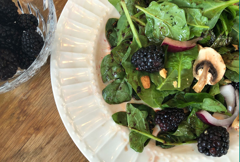 Closeup of a spinach salad with blackberries, in a large white bowl