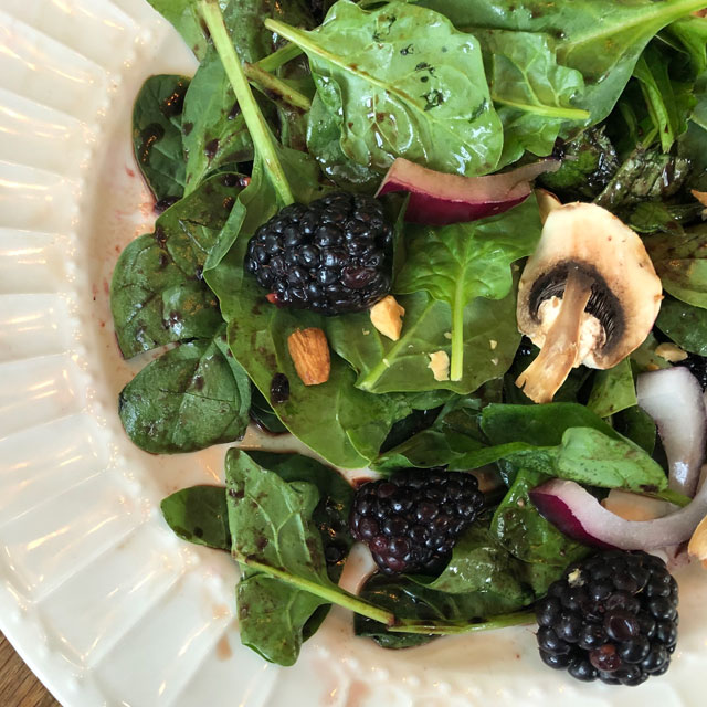 Closeup of fresh spinach salad with blackberries in a white salad bowl.
