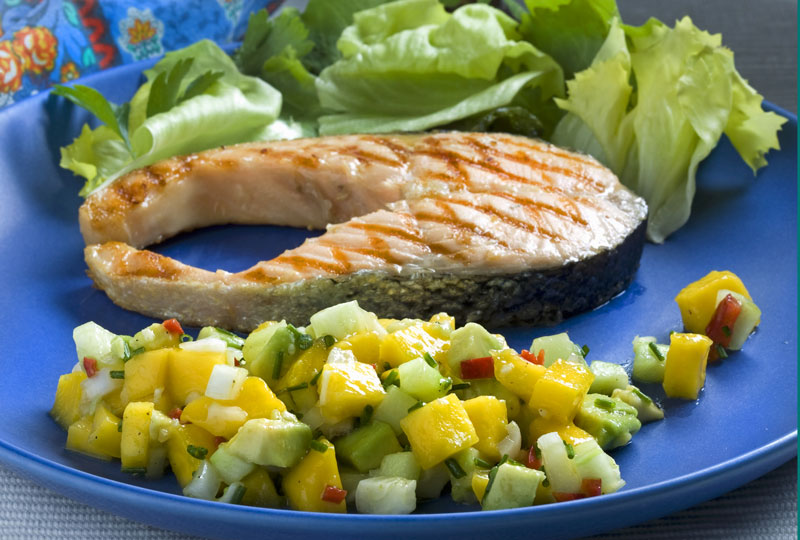 A grilled tuna steak plated with a mango-avocado salad on the side.