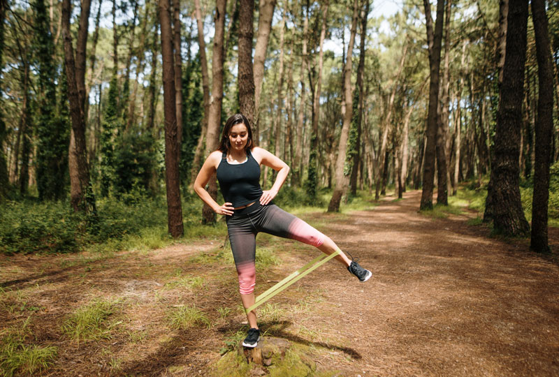 Woman working out in a forest with resistance band around her legs.