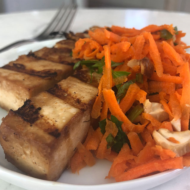 Grilled tofu steaks topped with carrot salad, plated and ready to serve.