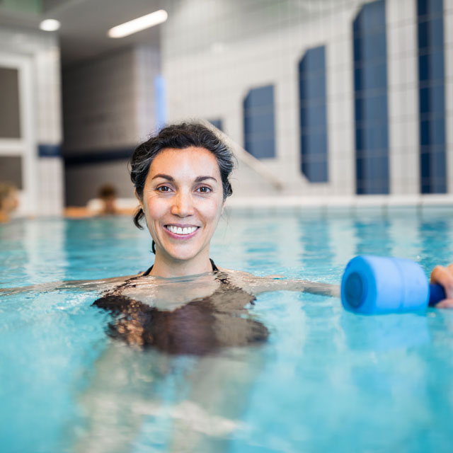 A woman exercises in an indoor swimming pool, holding two weights.