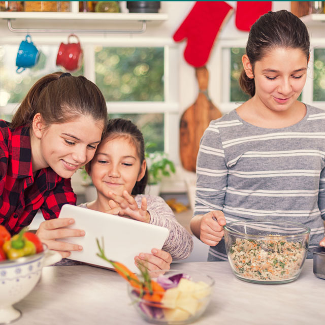 Three girls prepare stuffing and a turkey while using a tablet.