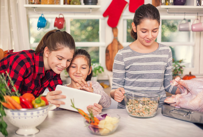 Three young girls prepare stuffing and turkey while checking an iPad