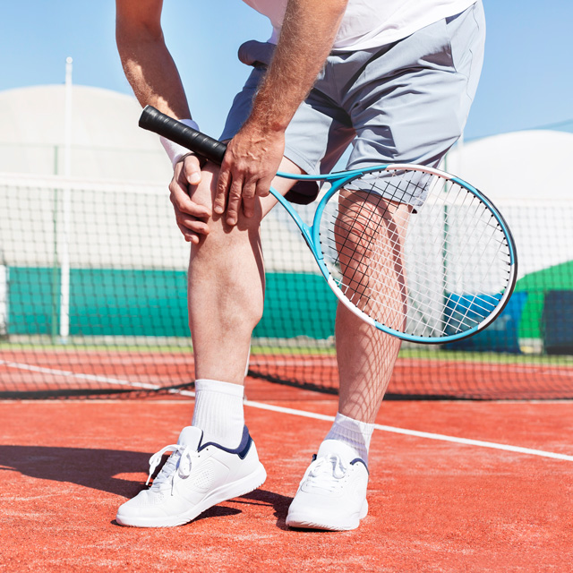 Male tennis player bending over with knee pain
