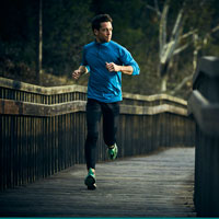 Man jogging outdoors on a wooden boardwalk through trees