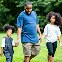 Older man walking hand-in-hand with a young girl on each side, outdoors.