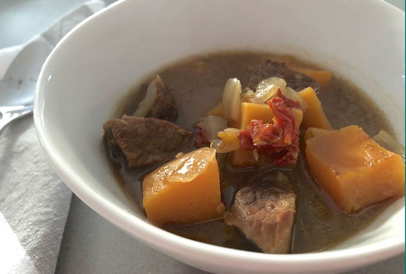 Beef stew with butternut squash and sun-dried tomato, served in a deep white soup bowl.