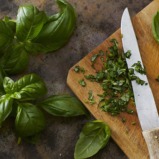 Fresh basil on a wood cutting board, some of it chopped small.