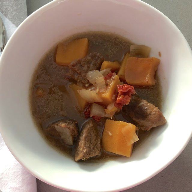 Beef stew with butternut squash and sun-dried tomato, served in a deep white soup bowl.