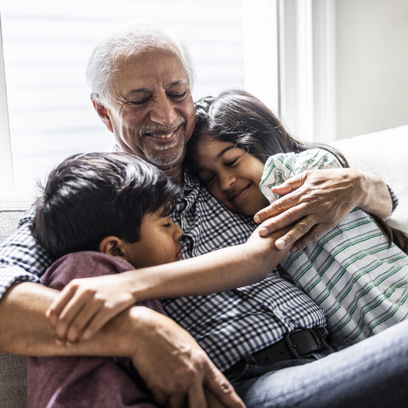 Grandfather cuddling with grandchildren on couch at home