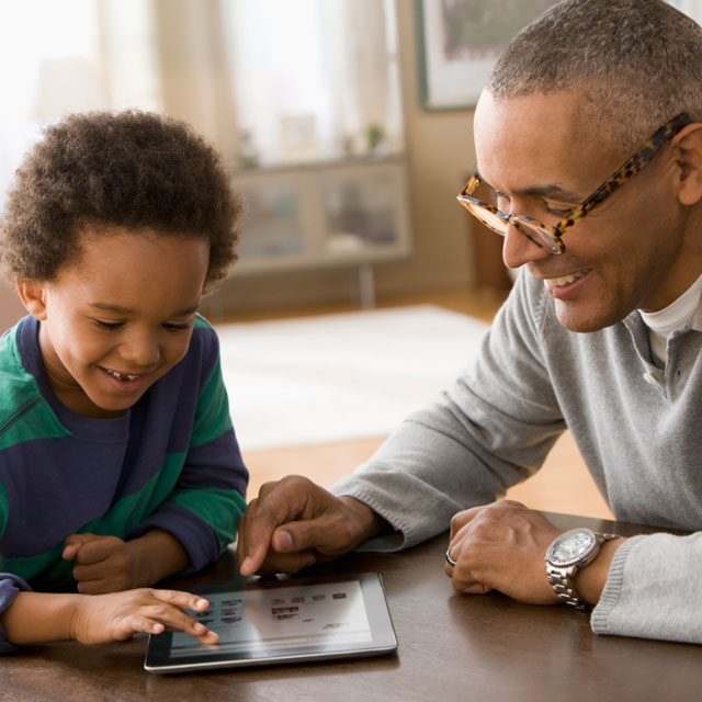 An older African-American man plays with a young African-American boy using a tablet computer.