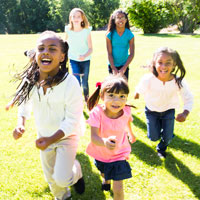 Five children run in an open field on a sunny day.