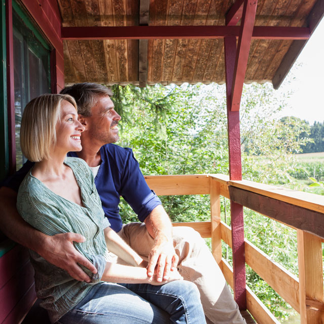 A middle aged couple sit on the deck of a mountain cabin.