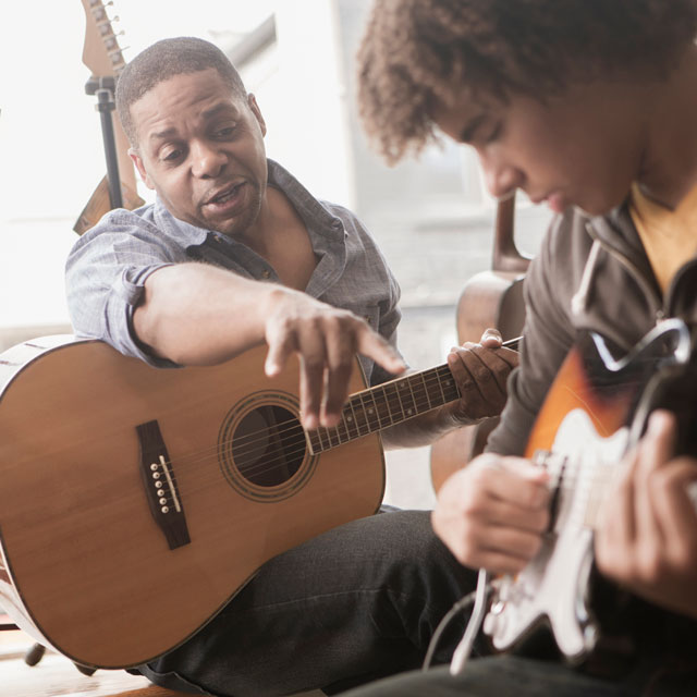 A middle-aged man and a young man play guitars together.