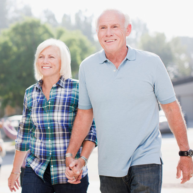 An older couple walk hand-in-hand along a residential street.
