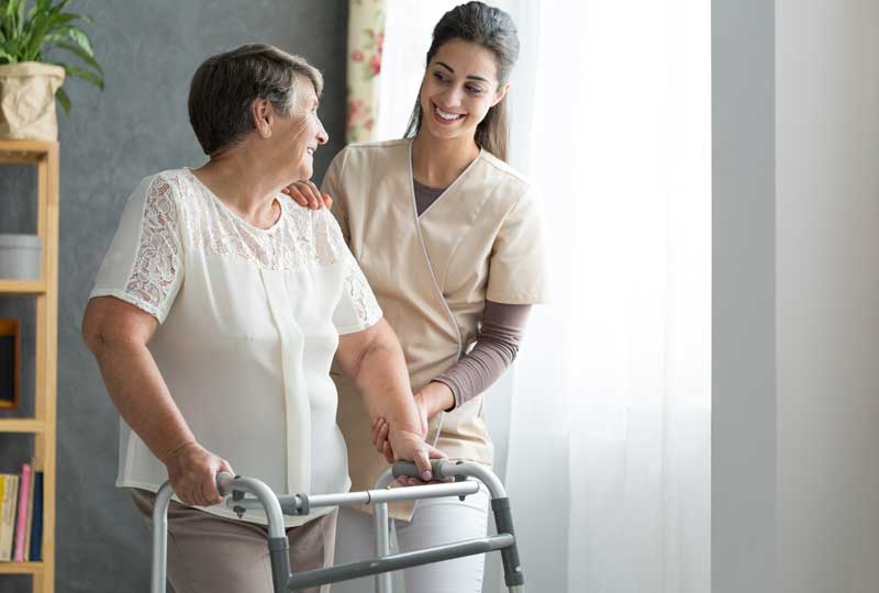 Woman strolling with walker, guided by nurse, recovering from anterior hip replacement surgery