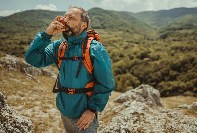 Man hiking on mountain, exercising with asthma inhaler