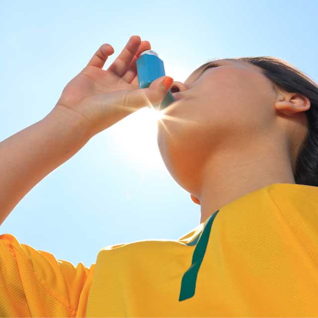 Child wearing sports jersey using asthma inhaler