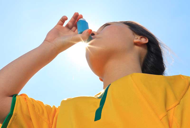 Child wearing sports jersey using asthma inhaler